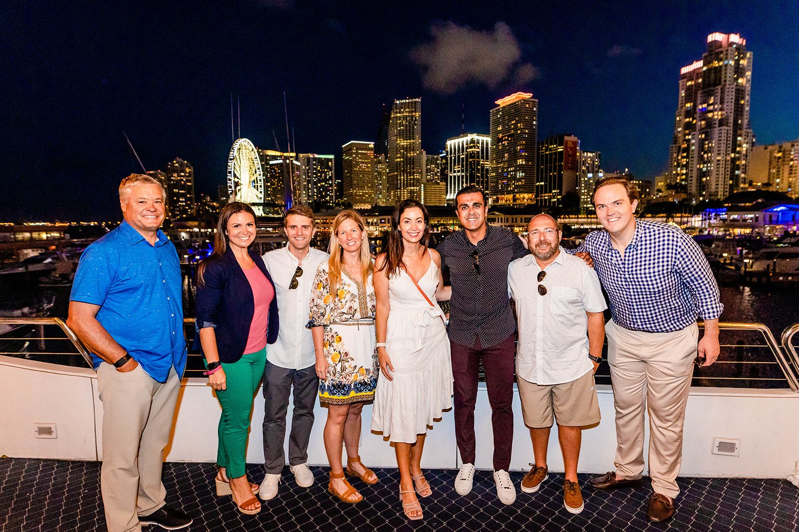 Company team posing together on deck at night with the illuminated downtown Miami skyline behind them
